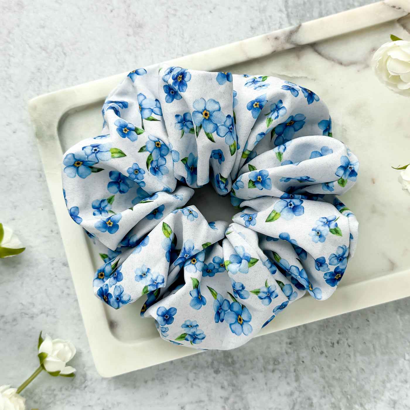 Floral patterned scrunchie on a marble surface with flowers around.