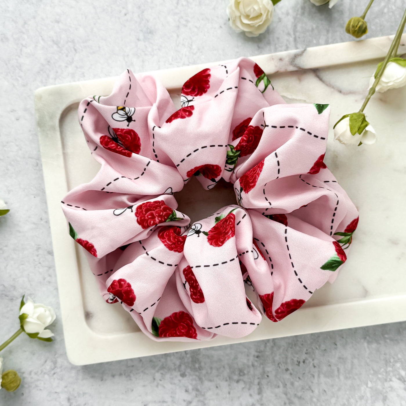 Pink scrunchie with red raspberry pattern on a marble surface.