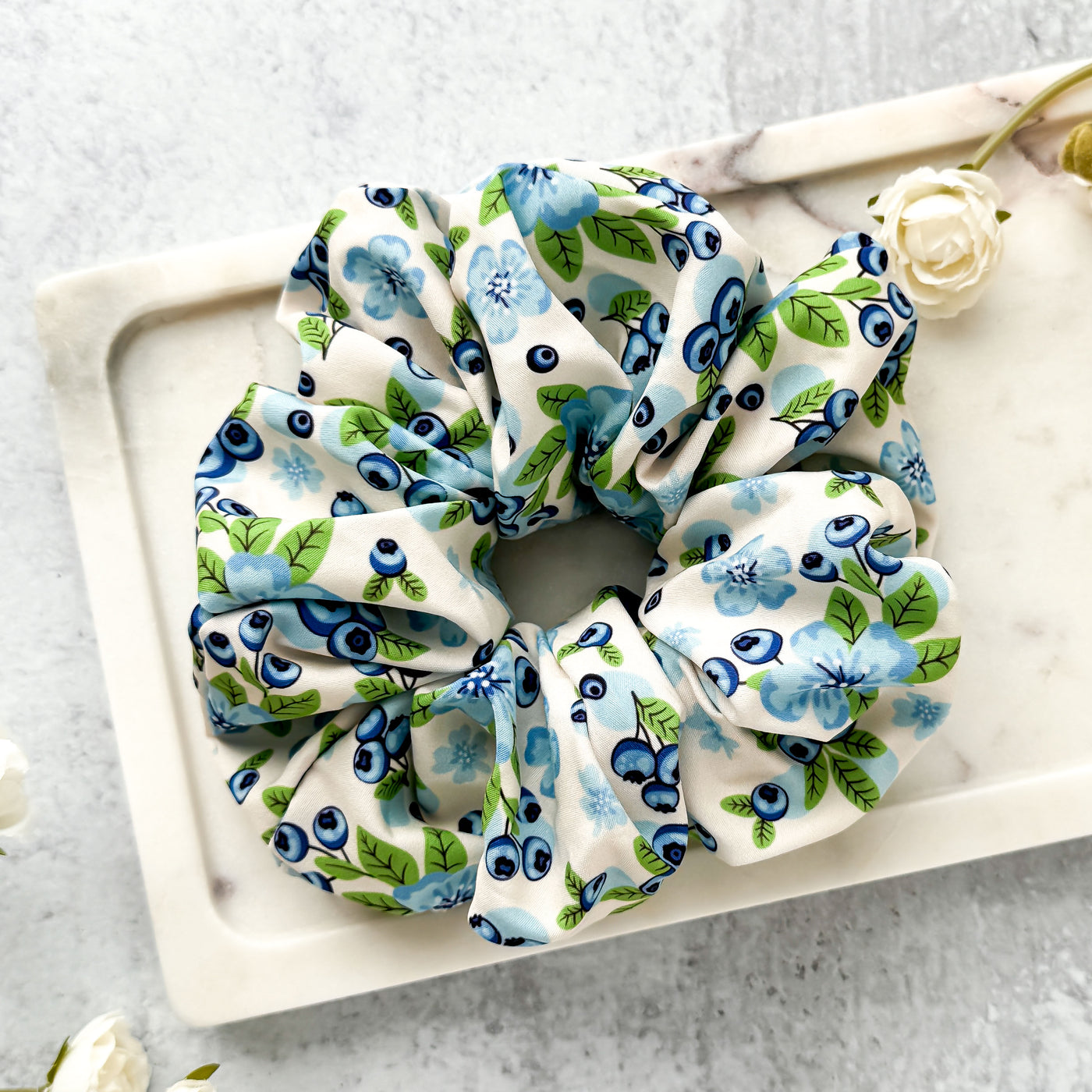 Floral scrunchie on a white tray with flowers in the background.
