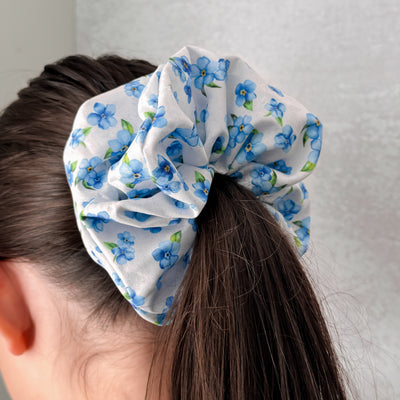Person wearing a large blue floral scrunchie on their hair against a plain background.