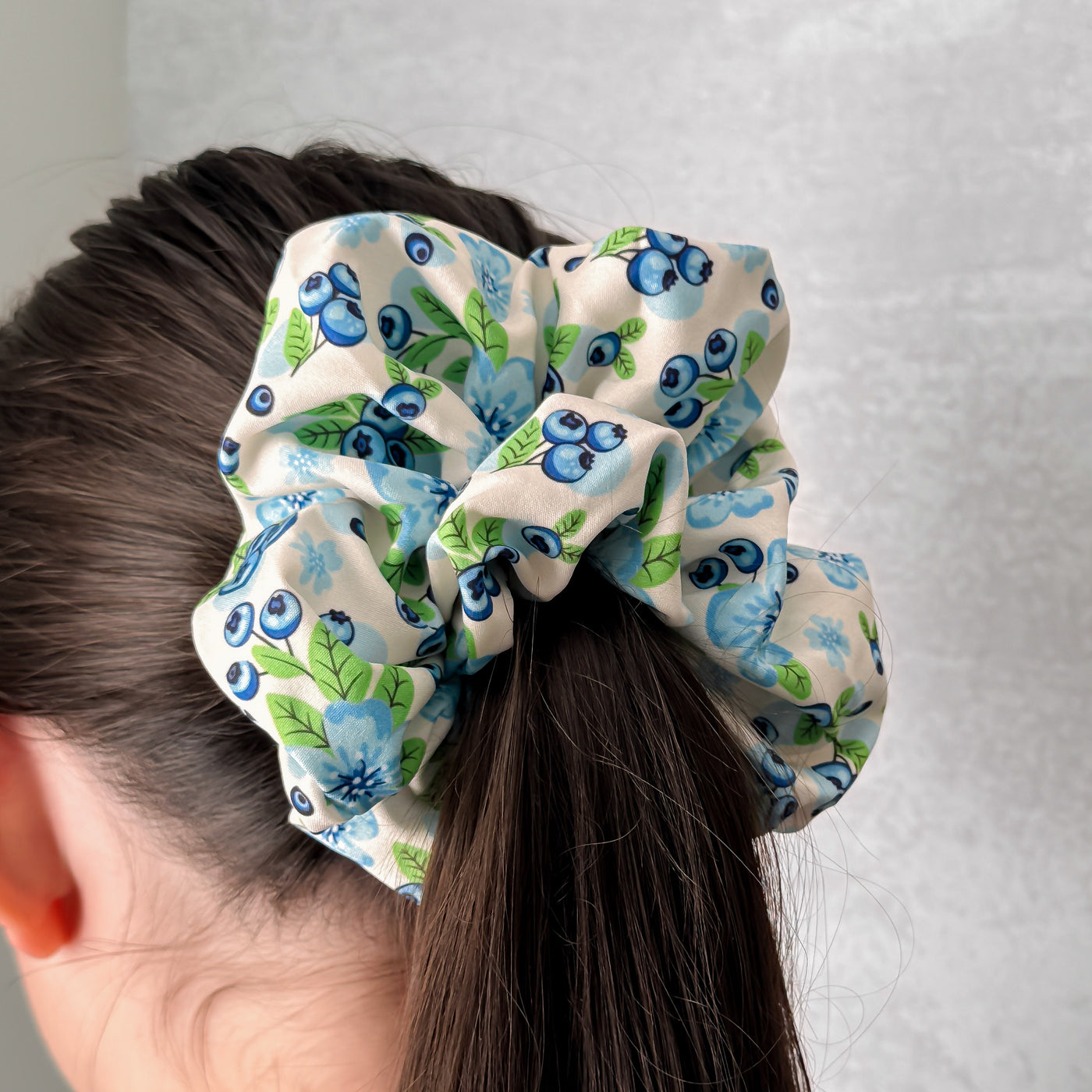 Scrunchie with blueberry pattern on a person's hair against a plain background.