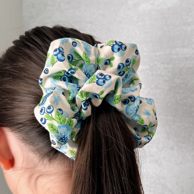 Scrunchie with blueberry pattern on a person's hair against a plain background.