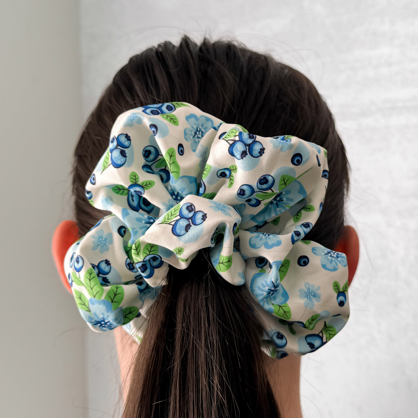 Person wearing a blueberry patterned scrunchie on a plain background.