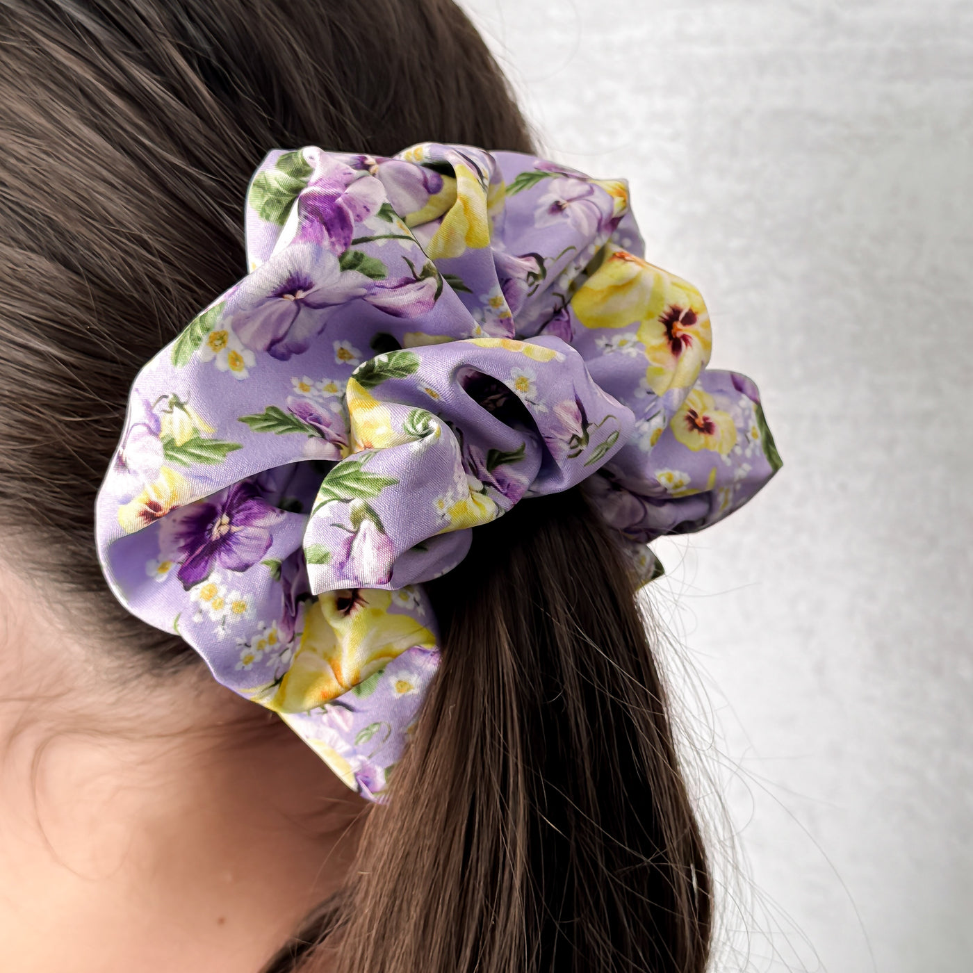 Floral scrunchie on a person's hair against a white background.