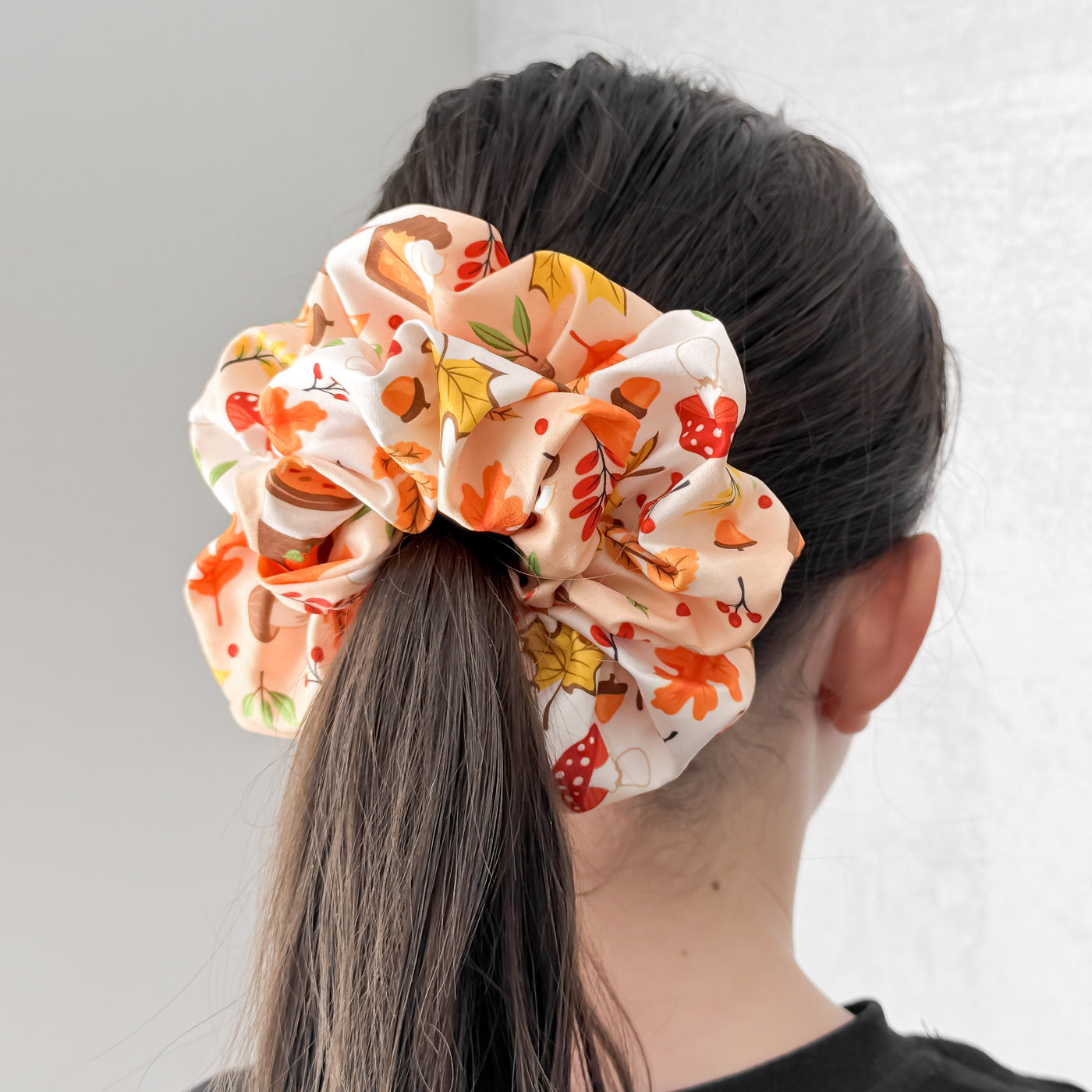 Person wearing a colorful scrunchie with autumn leaves on a plain background.