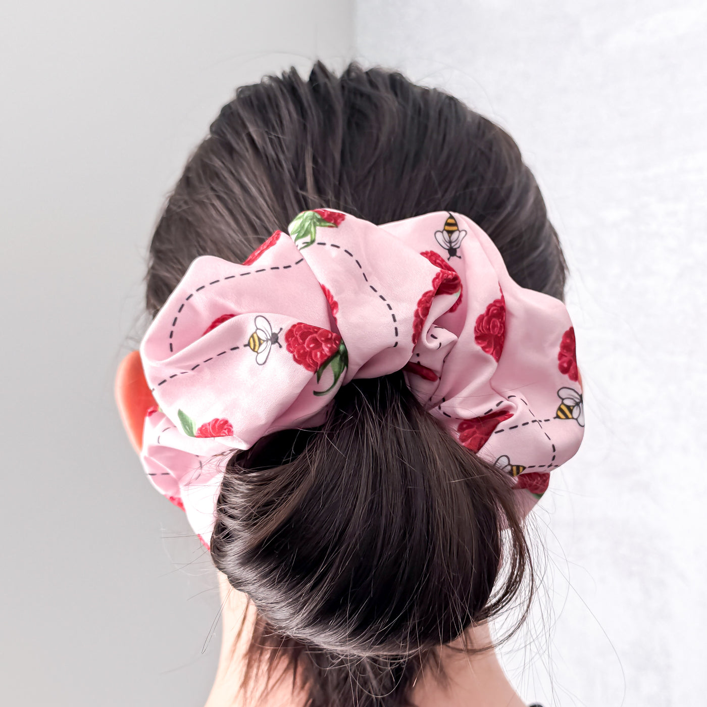 Person wearing a pink raspberry scrunchie on a plain background.