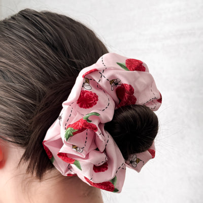 Pink raspberry scrunchie on a bun against a white background.