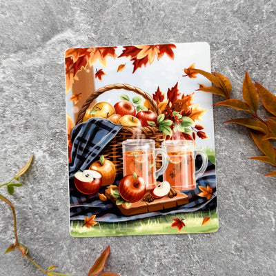 Decorative card with autumn theme featuring apples, a basket, and mugs on a textured surface.