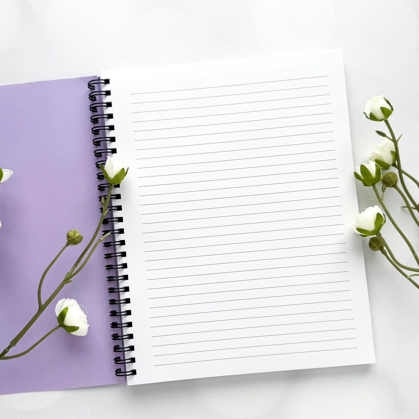 Open notebook with lined pages on a white background with purple cover and white flowers.