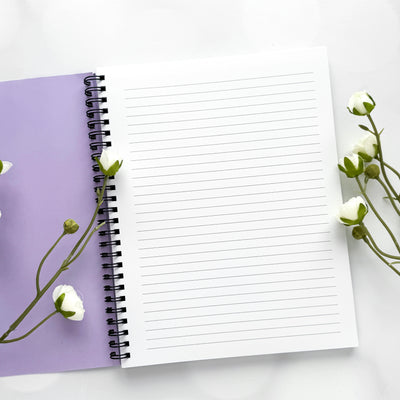 Open notebook with lined pages on a white background with purple cover and white flowers.