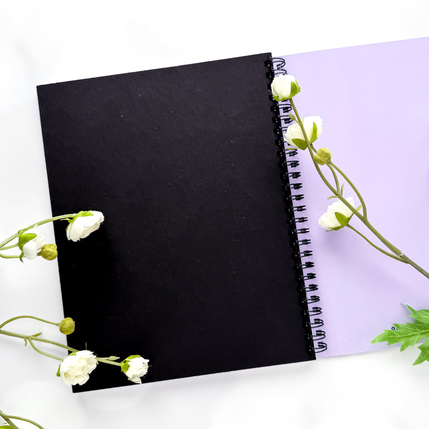 Black notebook with white flowers on a light purple background.