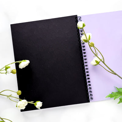 Black notebook with white flowers on a light purple background.