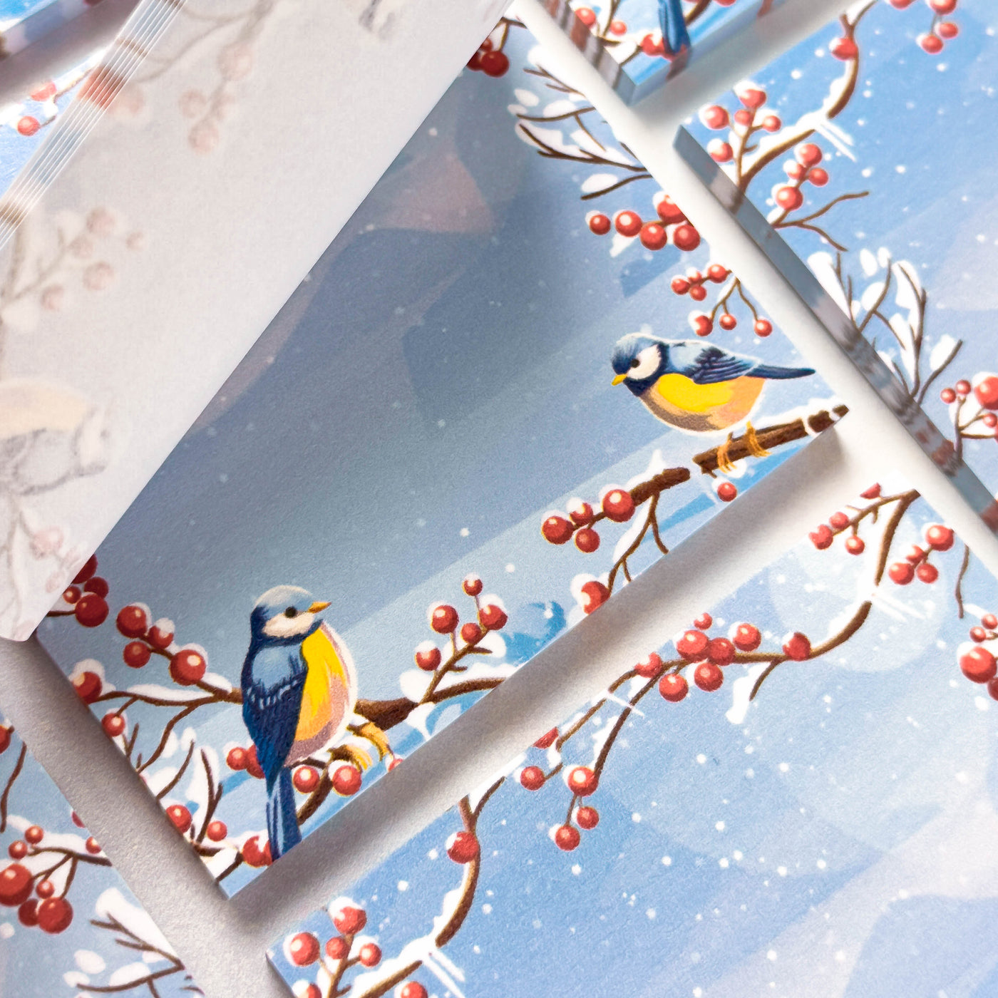 Two birds perched on a branch with red berries against a snowy landscape.