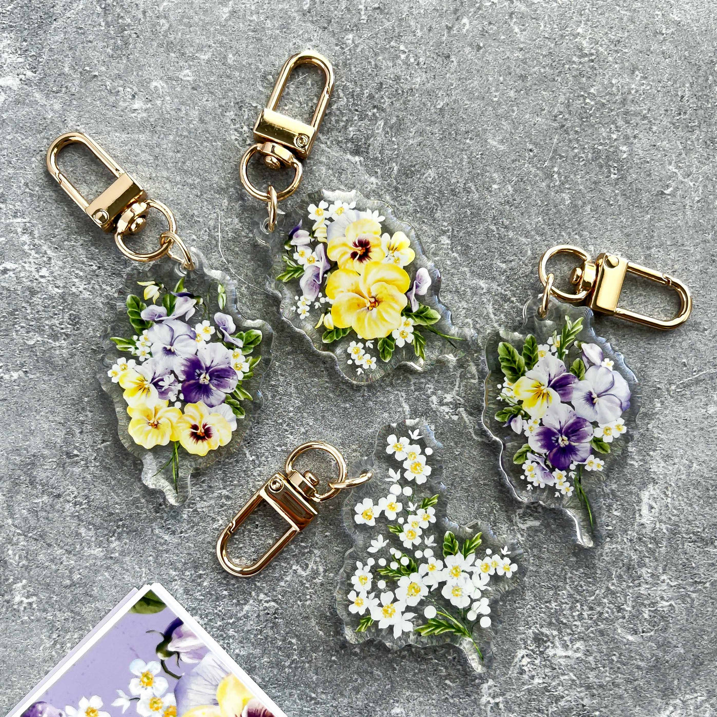 Floral keychains with clear holders on a gray surface.
