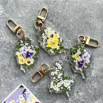 Floral keychains with clear holders on a gray surface.