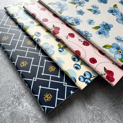 A collection of four mini notebooks with different covers, including a geometric pattern, a floral pattern, and two with red and blue designs.