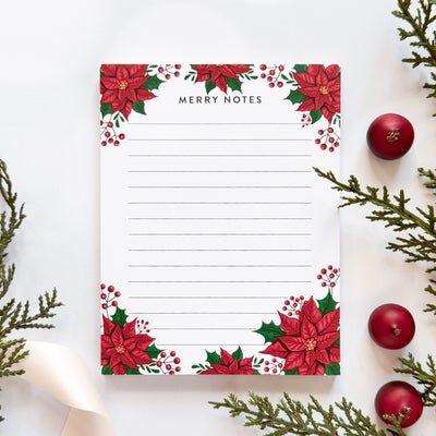 Merry Notes notepad with poinsettia design surrounded by Christmas decorations on a white background.