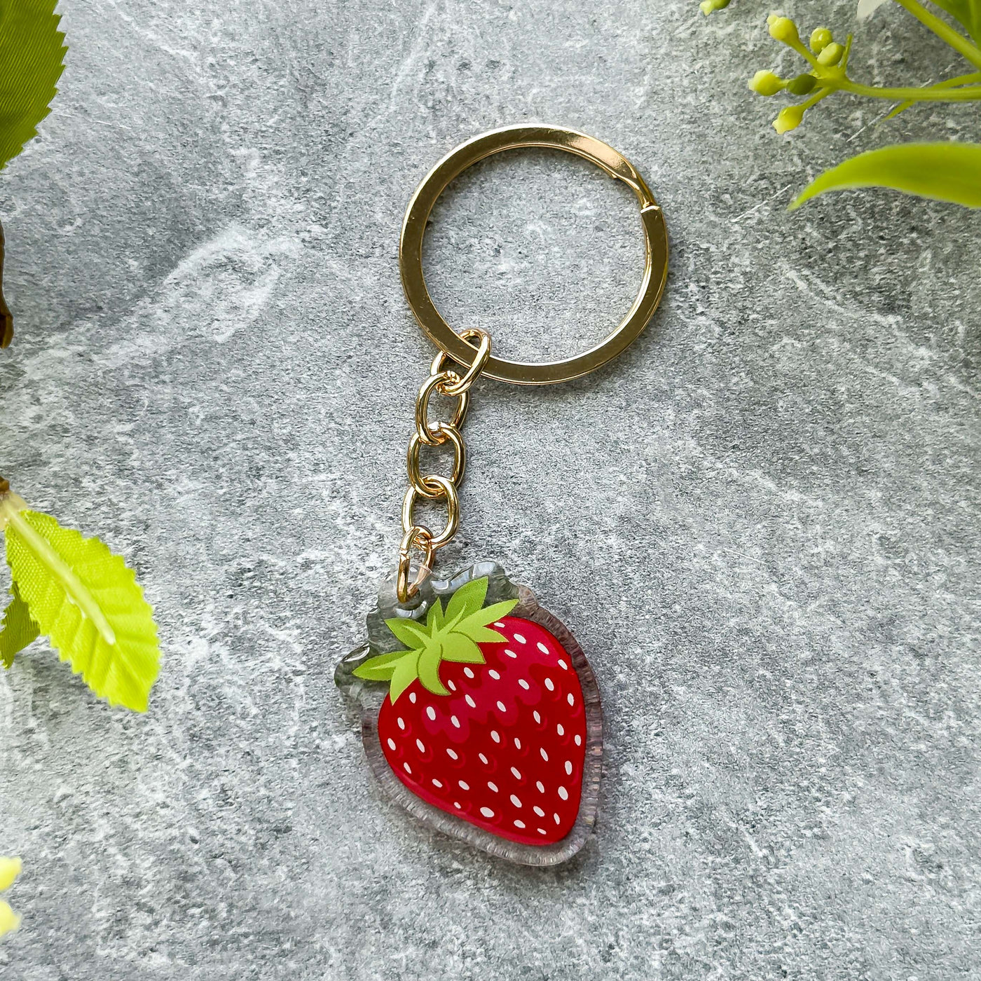 Strawberry-shaped keychain on a textured surface with green leaves.