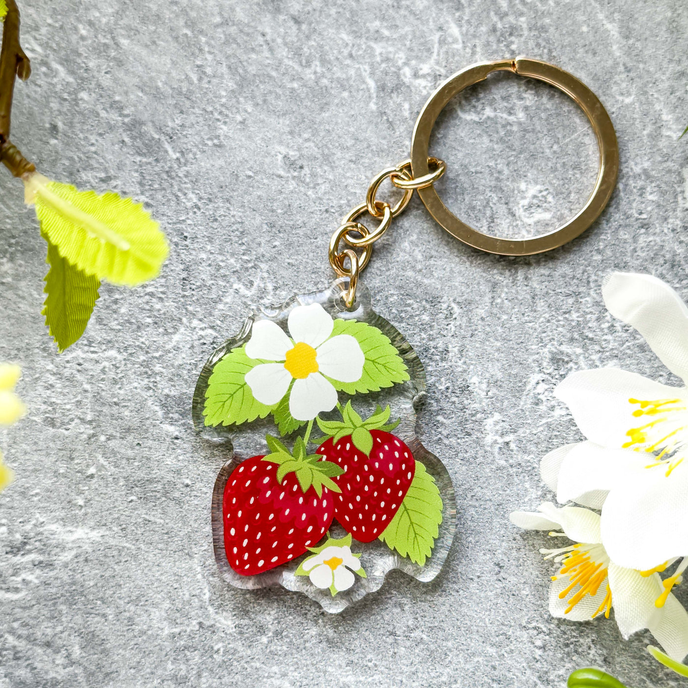Keychain with strawberries and flowers on a textured surface.