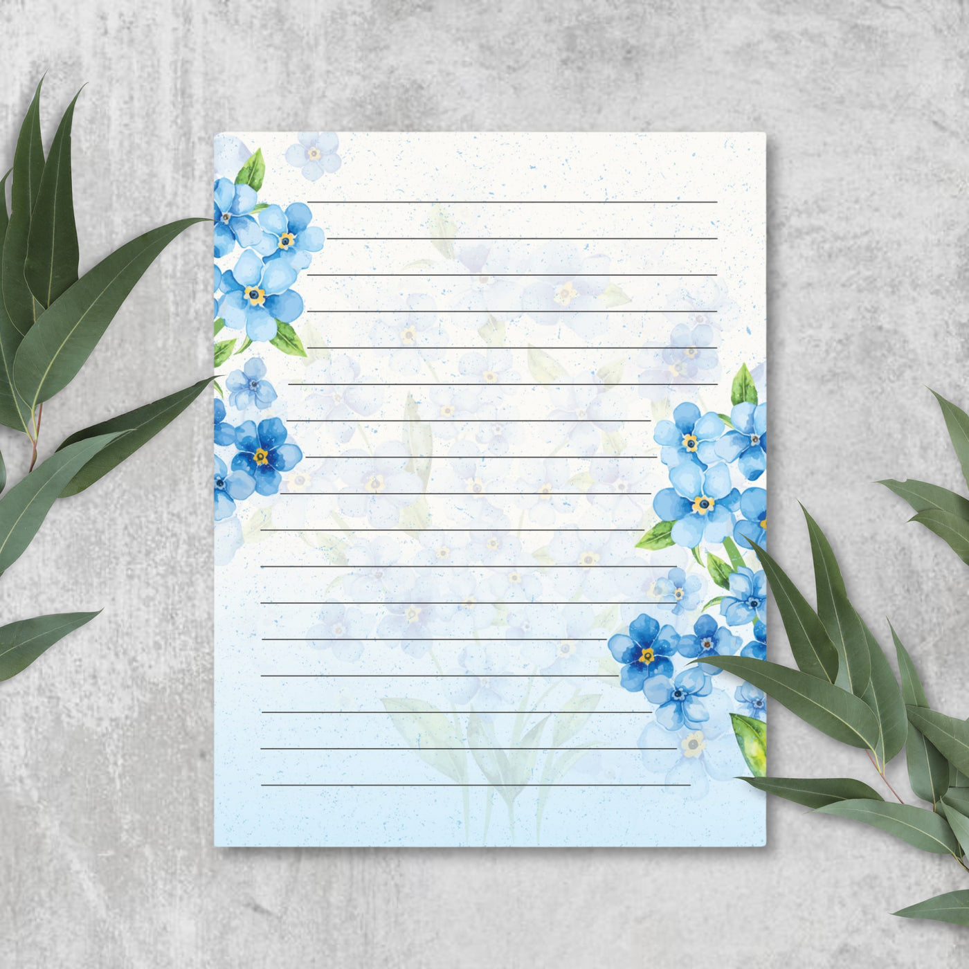 Notebook with blue floral design on a gray surface with green leaves.