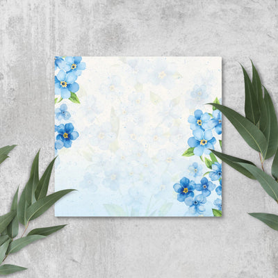 Sticky notes with blue floral design on a gray surface with green leaves.